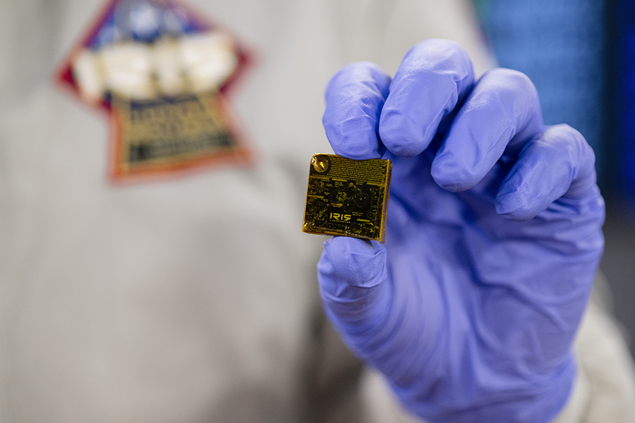  A hand wearing a purple glove holds a gold square with the word Iris etched on it.